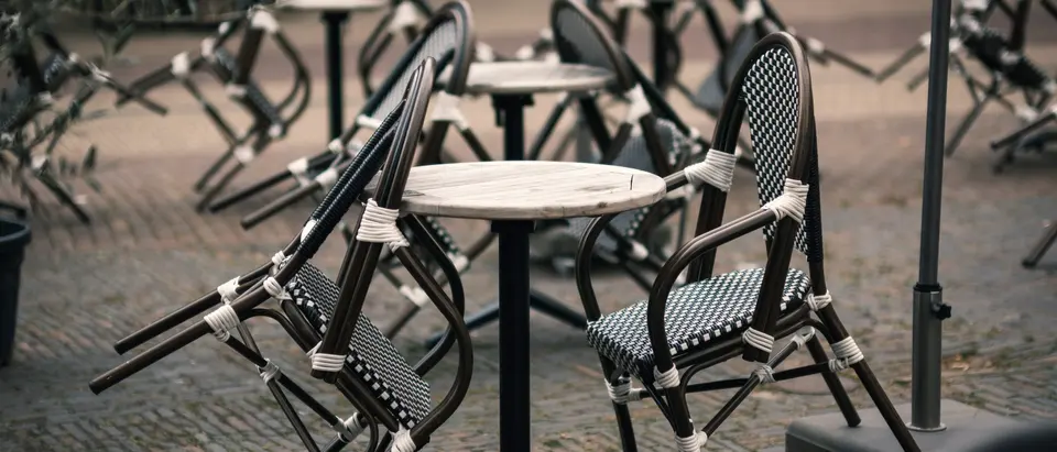Zusammengeklappte Bistrostühle an runden Tischen auf Kopfsteinpflaster, Terrasse vor dem Öffnen.