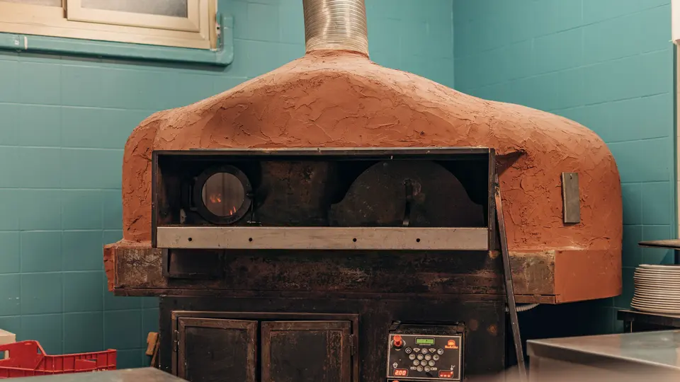Kuppelförmiger Steinofen mit brennendem Feuer in einer kleinen Pizzeria, türkis gefliester Raum.